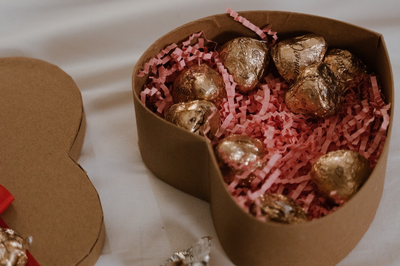 A heart-shaped box of chocolates open on a cream colored linen