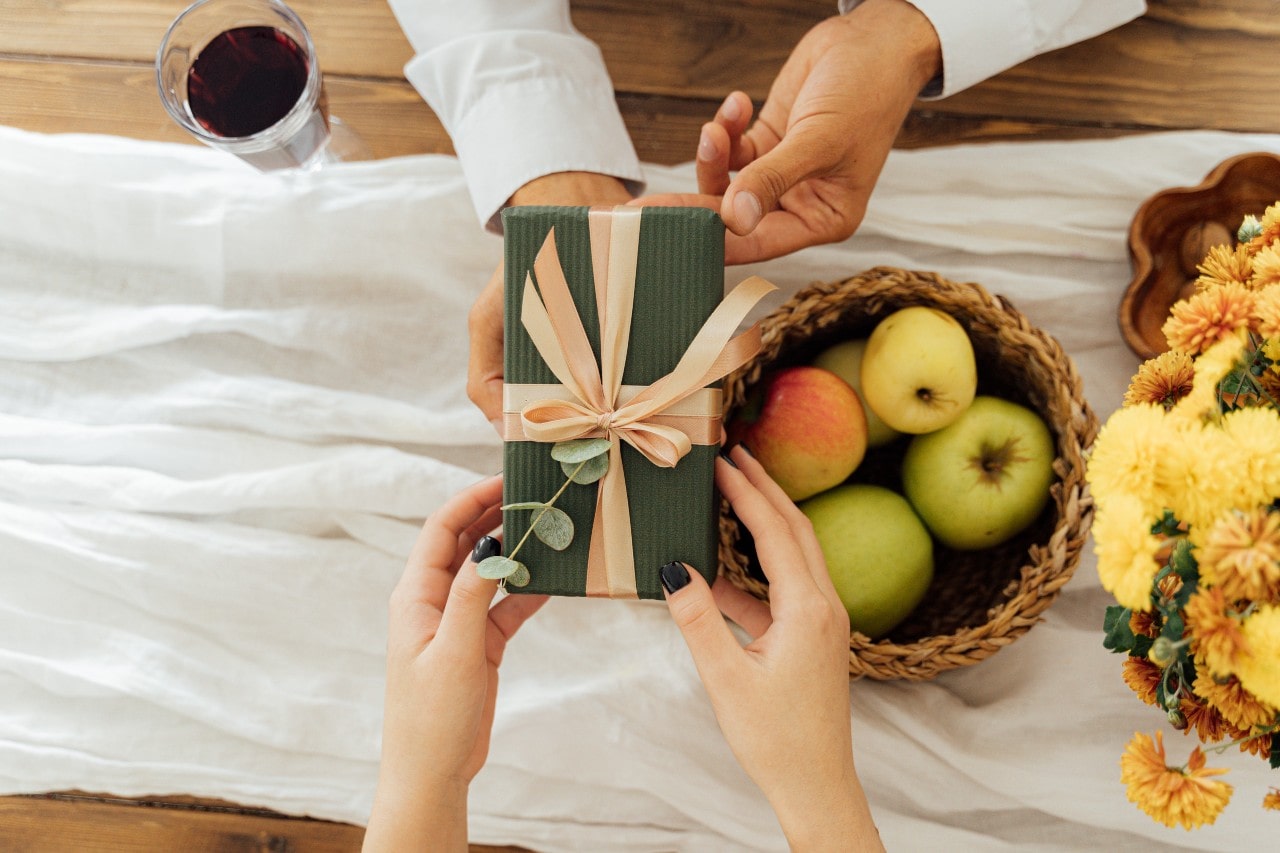 A man hands a woman a green wrapped gift box during a picnic
